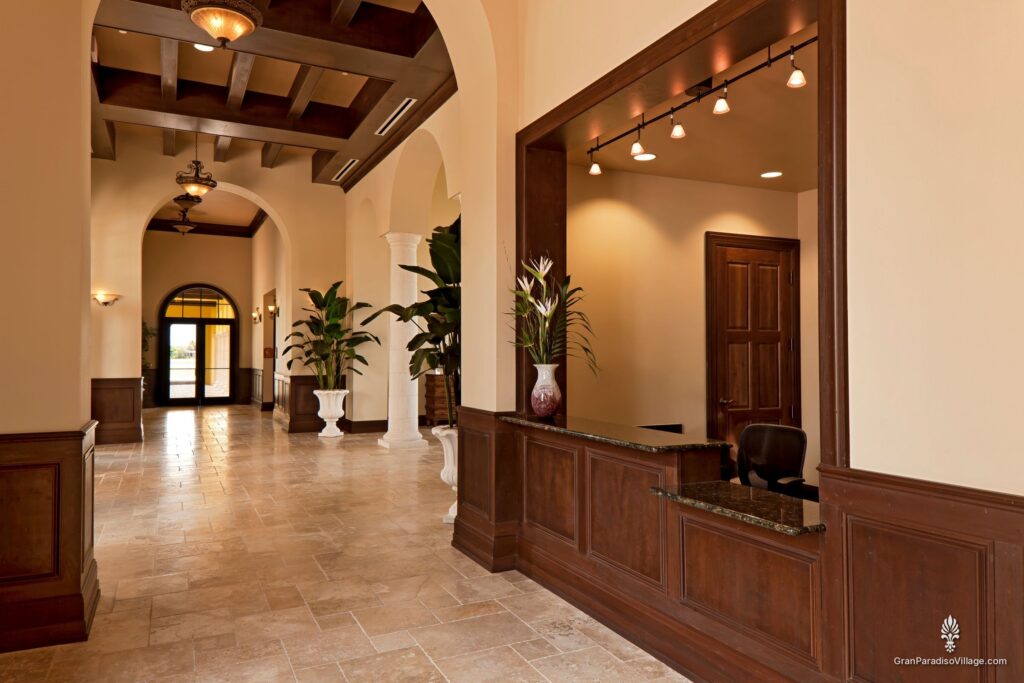 Main clubhouse gallery with stone floors, potted palms and the wood-paneled management office counter
