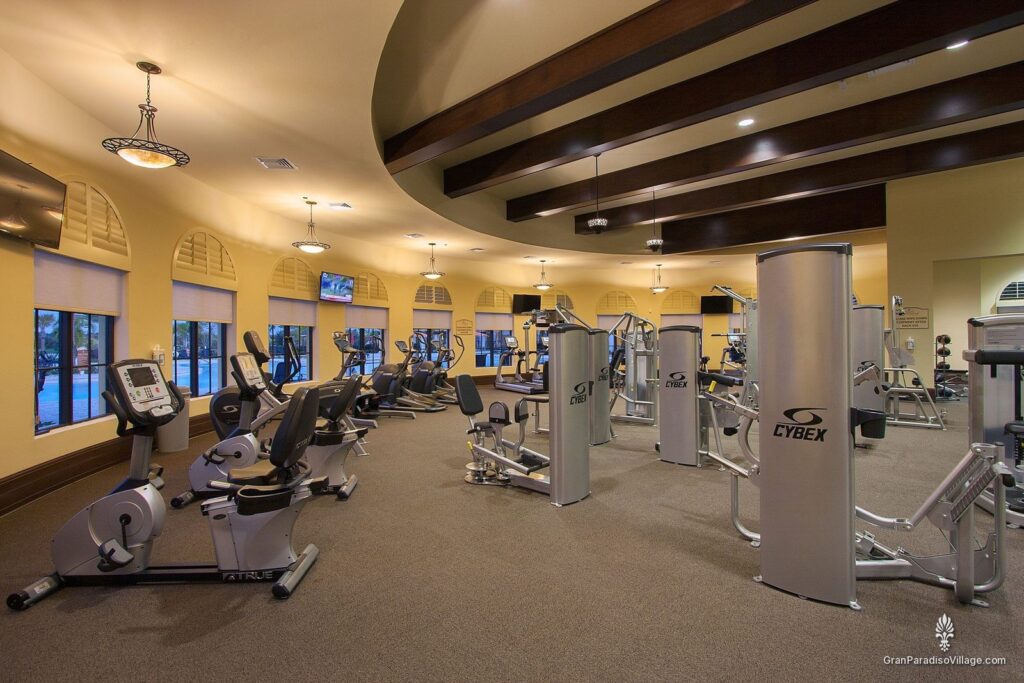 Fitness center with rows of cardio machines and strength equipment beneath arched windows