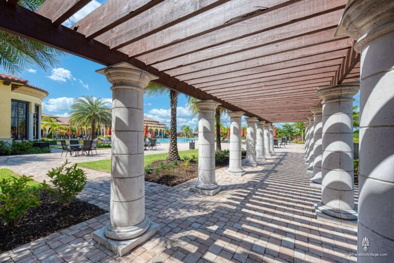 Wood pergola on white stone columns shading a paver walkway that leads to the pool
