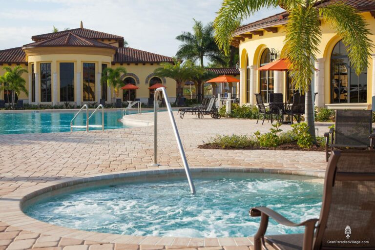 Round spa with a handrail beside the resort pool, shaded by palms and orange umbrellas