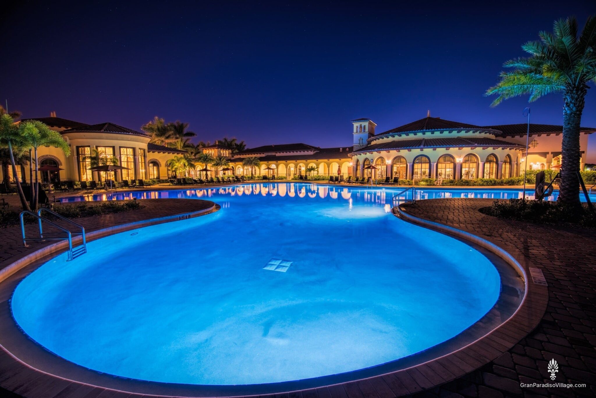 Resort pool glowing blue at twilight, with the lit clubhouse arches behind it