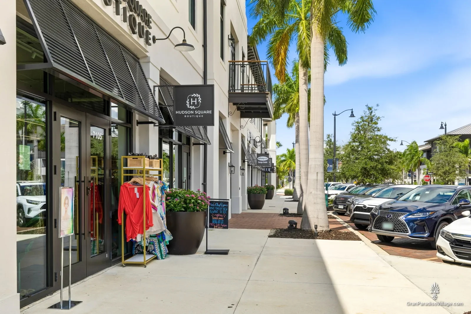 Downtown Wellen sidewalk with a clothing rack outside a boutique, flower planters and royal palms