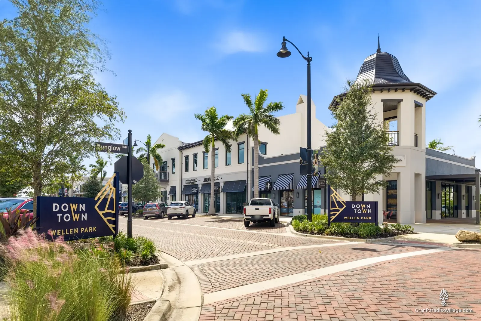 Downtown Wellen Park entrance sign at Sunglow Boulevard with palm trees, shops and a cupola-topped corner building