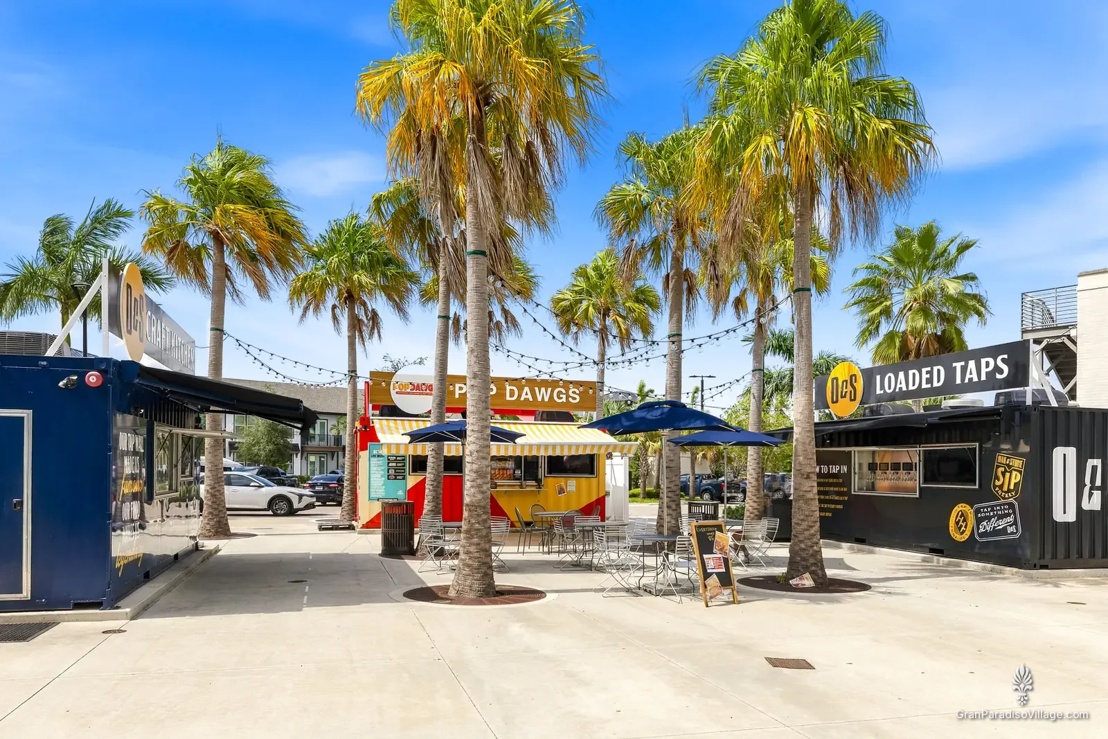 Downtown Wellen food-truck court with container kitchens, string lights, blue umbrellas and tall palms