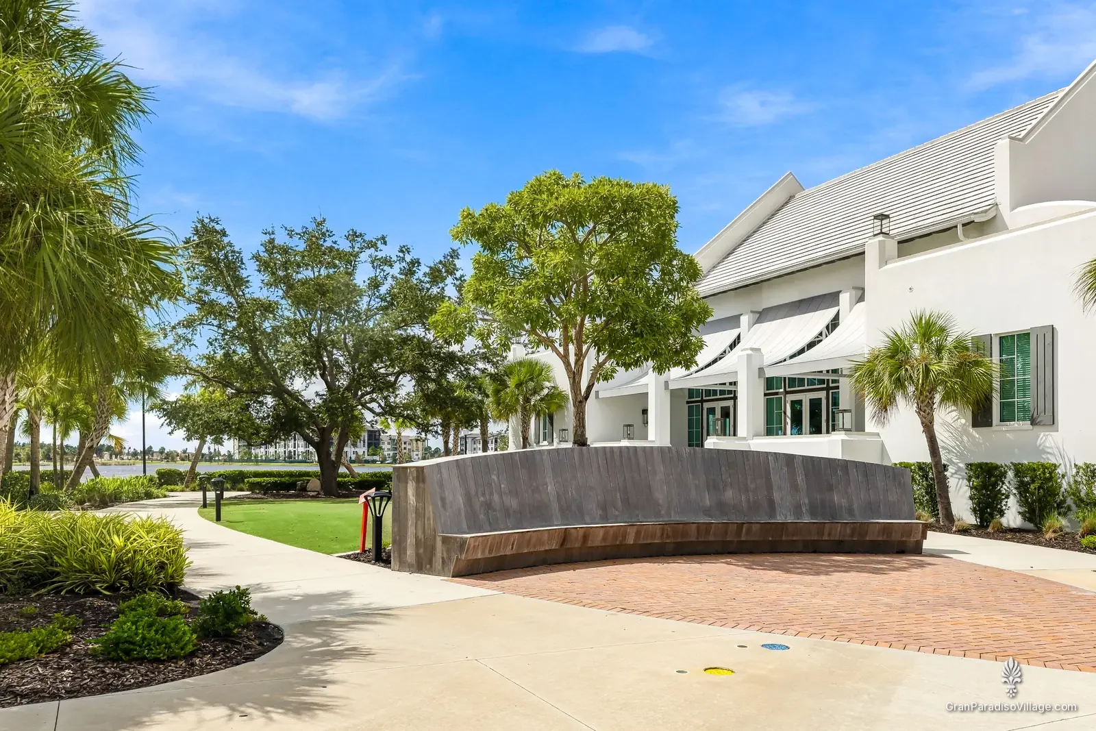 Curved stone seat wall, brick paving and live oaks beside a white lakefront building in Downtown Wellen