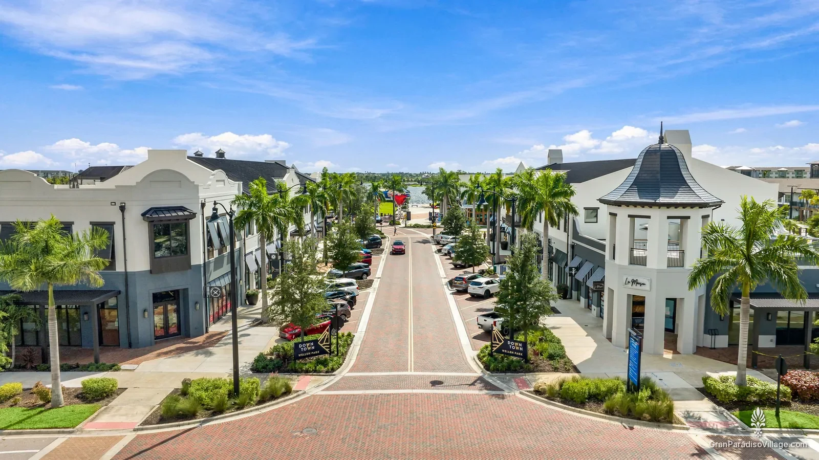 Aerial view down a palm-lined Downtown Wellen street of shops and restaurants toward the Grand Lake, Wellen Park, Florida