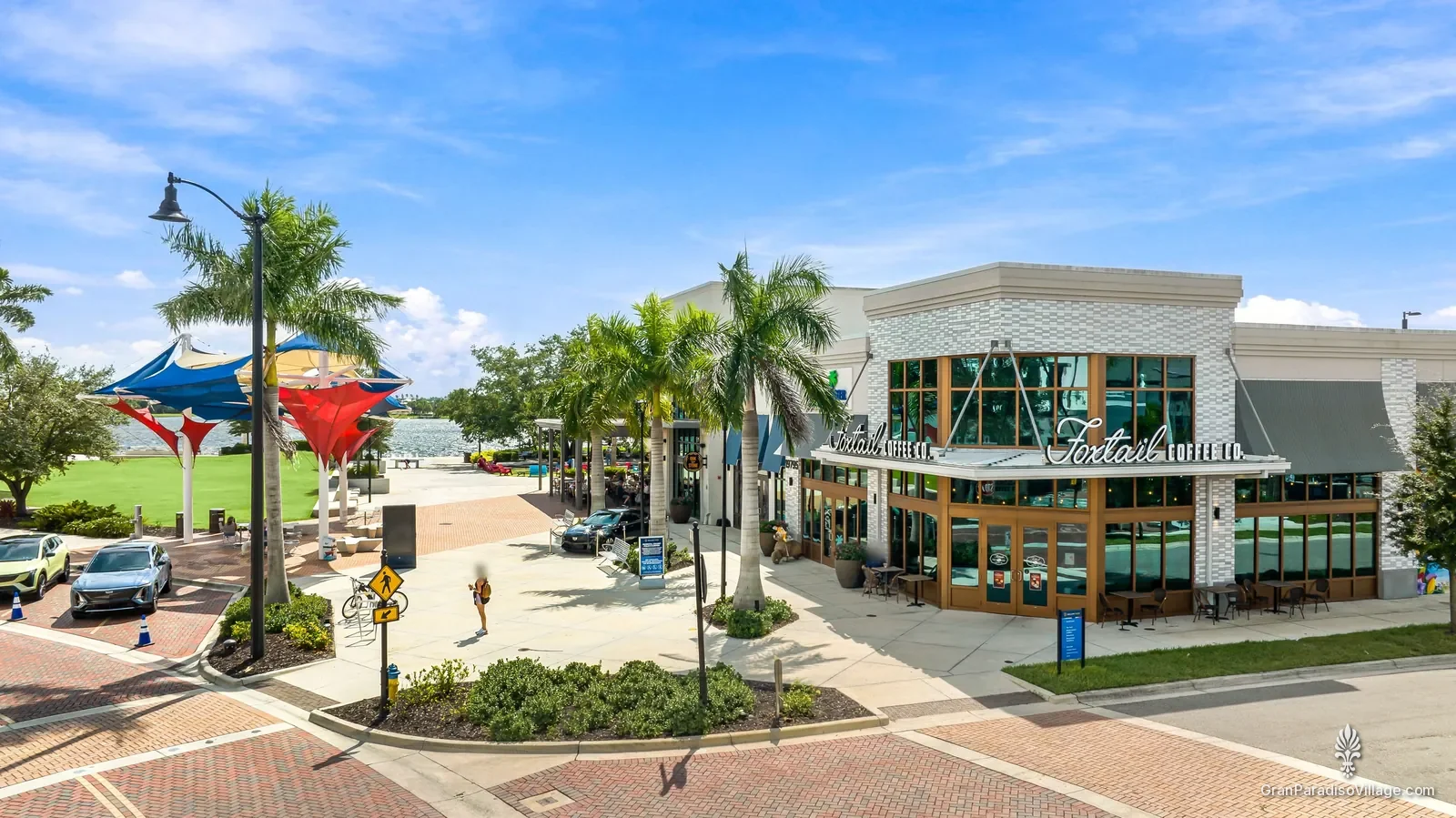 Elevated view of a Downtown Wellen corner with Foxtail Coffee, shade sails, palms and the Grand Lake beyond