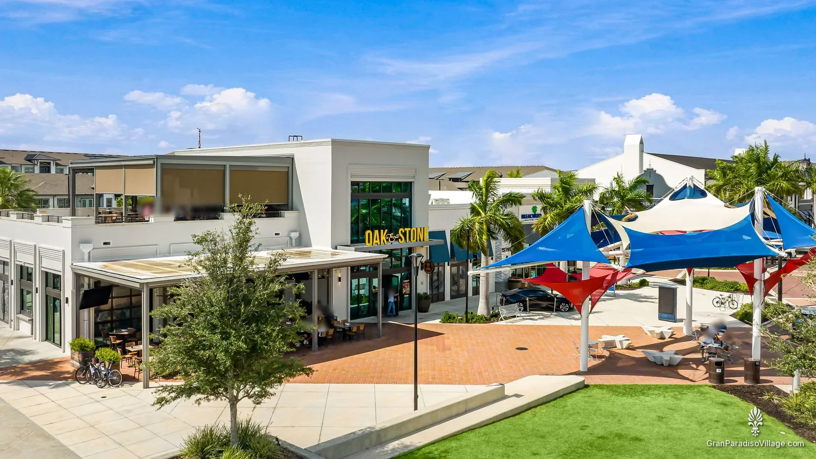 Downtown Wellen plaza with red, white and blue shade sails beside Oak & Stone restaurant and its rooftop patio