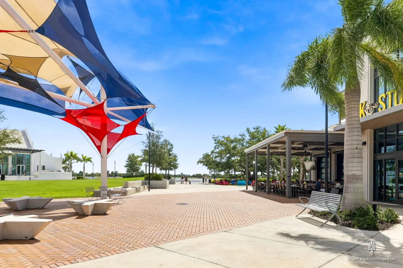 Red, white and blue shade sails over a Downtown Wellen plaza with the lawn and Grand Lake beyond