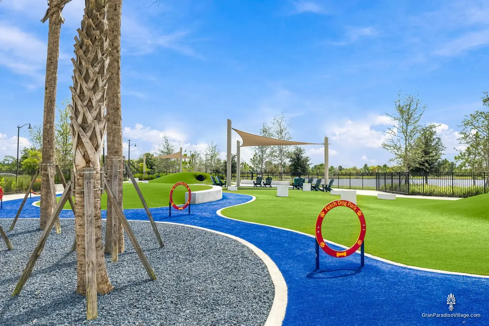Agility hoop on turf beside a blue path at Fetch Dog Park, with shade structures and palms