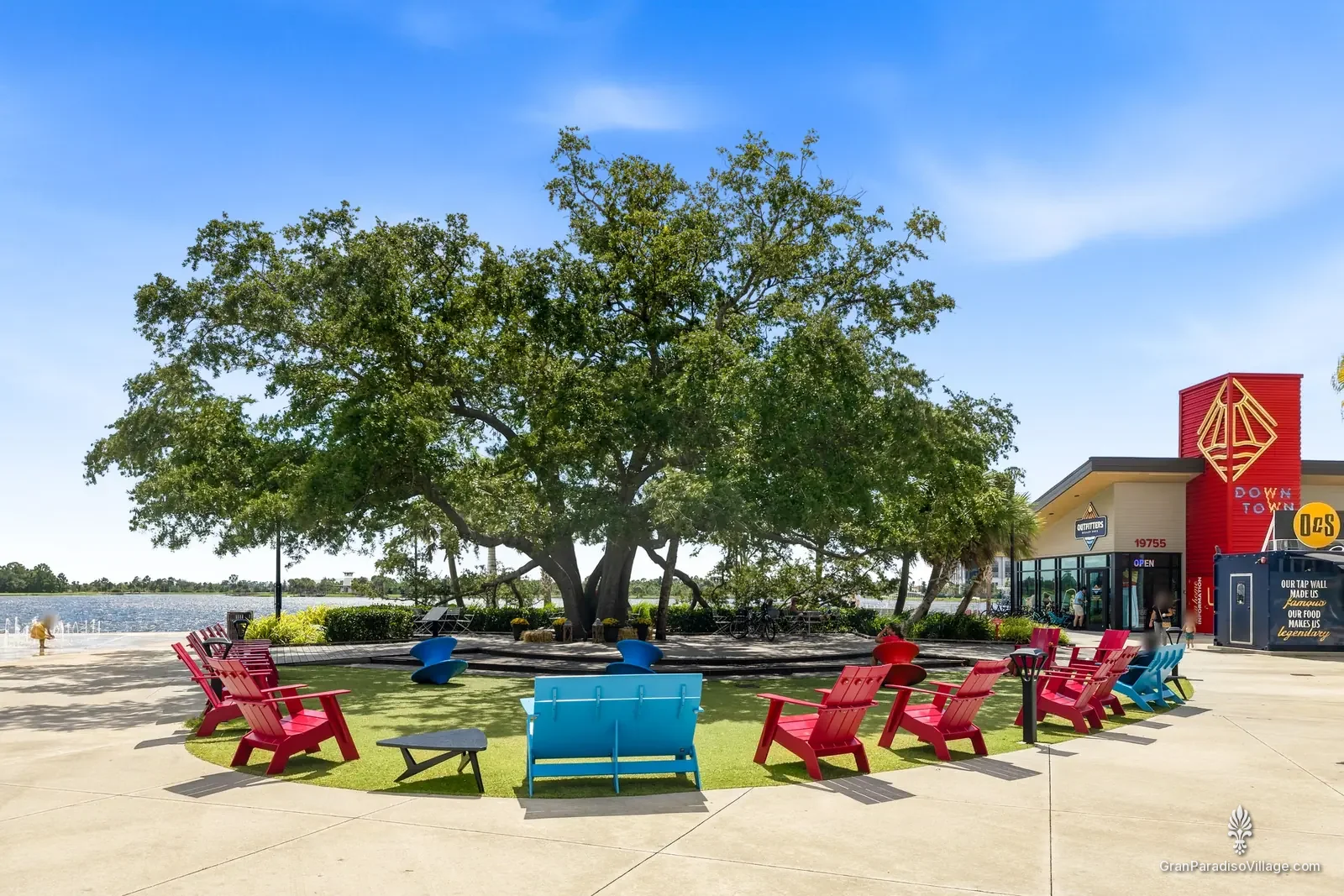 Red and blue Adirondack chairs in a circle under the Heritage Tree, with the Grand Lake and the red Outfitters tower