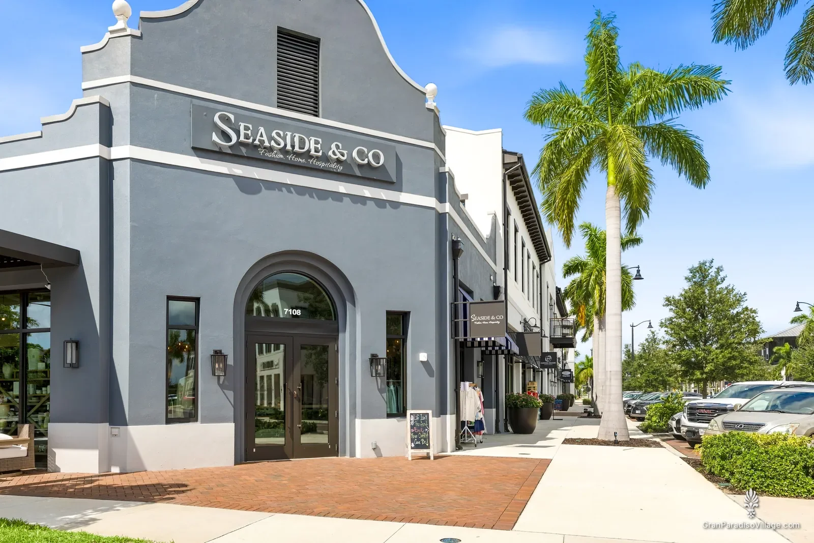 Gray Dutch-gable storefront of Seaside & Co. with a palm-lined sidewalk in Downtown Wellen