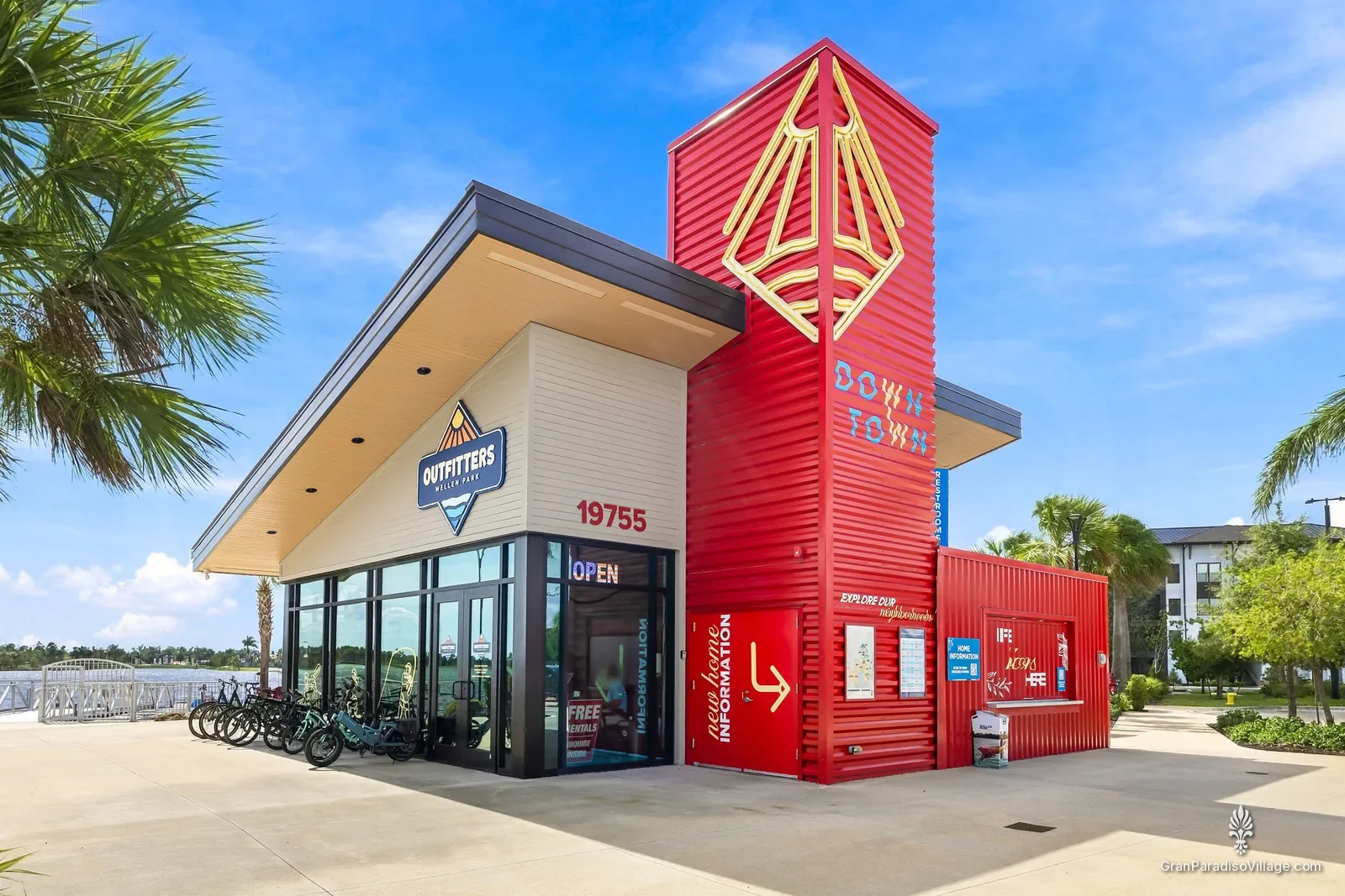 Wellen Park Outfitters building with its red Wellen-logo tower and a row of rental bikes beside the Grand Lake in Downtown Wellen
